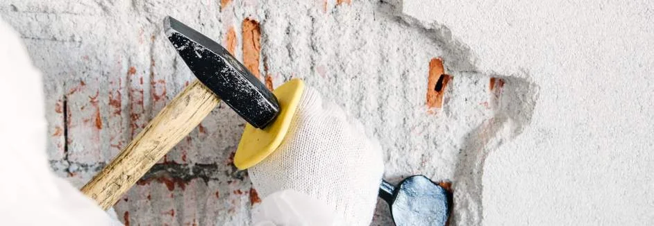 Hand mit Hammer und Meißel entfernt Putz von Wand
