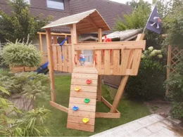 Hölzernes Spielgerät in Form eines Piratenschiffs mit Rutsche und Kletterwand.
