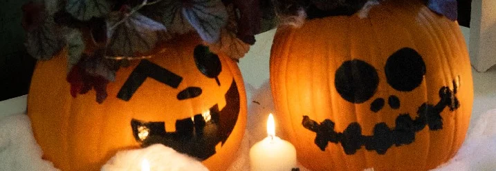 Zwei leuchtende Halloween-Kürbisse mit Kerzen und Spinnen dekoriert.