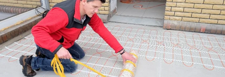 Person verlegt Fußbodenheizung auf einem Balkon.