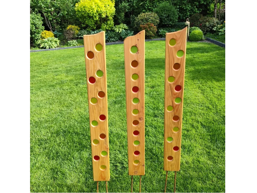 Drei hohe Holzlatten mit bunten Glaskreisen im Rasen