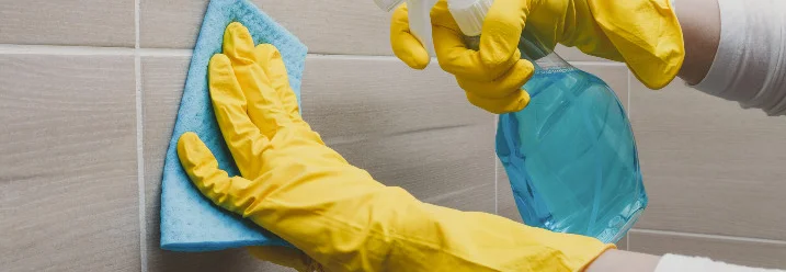 Person reinigt Fliesen mit Spray und Lappen.