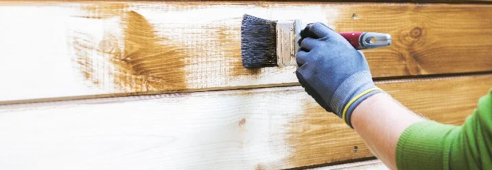 Person streicht Holzfassade mit Pinsel