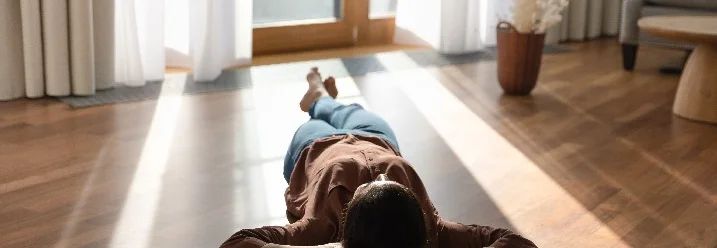 Person liegt auf dem Rücken auf einem Holzboden.
