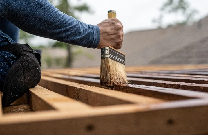 Person streicht Holzbalken mit Pinsel