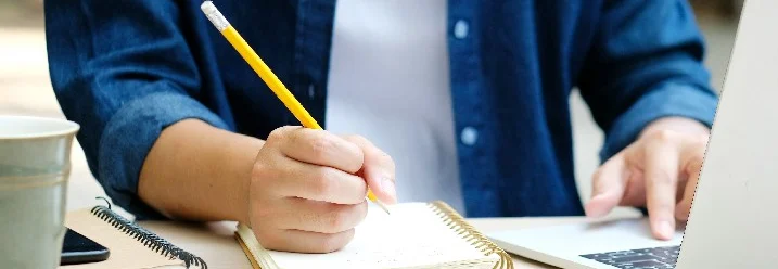 Person schreibt mit Bleistift in Notizbuch
