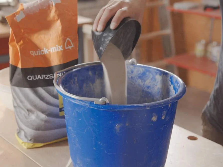 Person schüttet Quarzsand in einen Eimer.