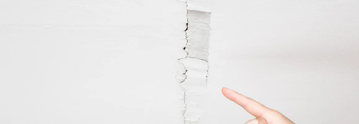 Hand zeigt auf Riss in weißer Decke