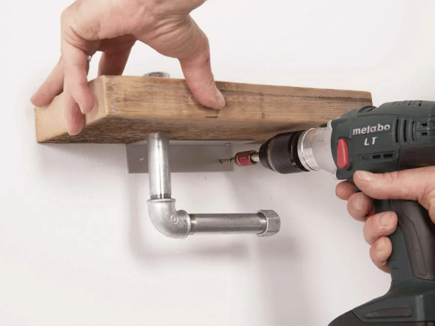 Person befestigt Holzbrett mit Bohrmaschine an Wand