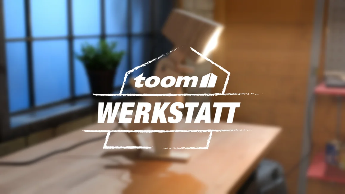 toom Werkstatt Logo mit unscharfer Nachttischlampe im Hintergrund