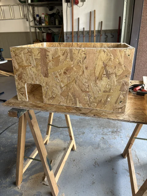 Ein selbstgebautes Kleintierhaus aus OSB-Platten steht auf zwei Sägeböcken.