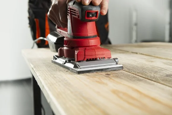 Person schleift Holz mit Schwingschleifer