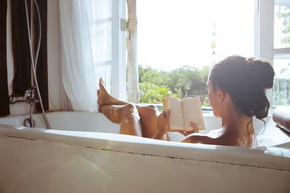 Person liegt in Badewanne und liest Buch