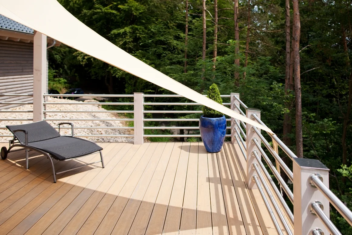 Leere Holzterrasse mit Sonnensegel und bepflanztem Topf
