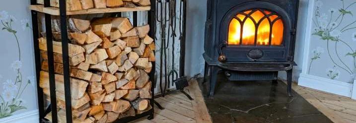 Ein Kaminofen mit brennendem Feuer neben einem Regal mit Brennholz.