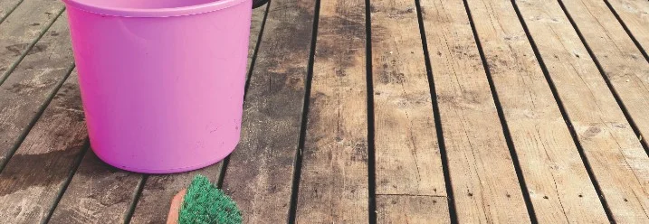 Ein rosa Eimer und eine Bürste auf einer Holzterrasse.