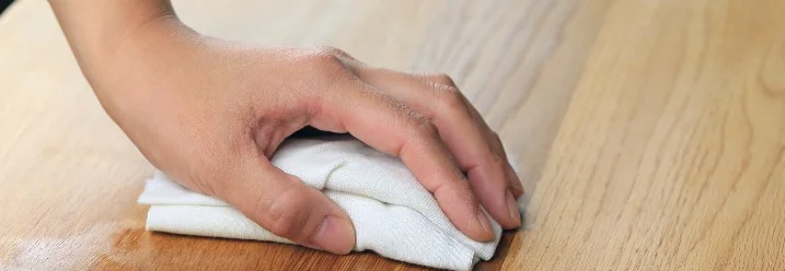 Hand reinigt Holztisch mit Tuch
