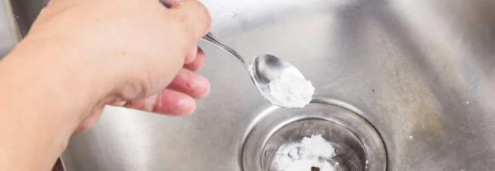 Hand schüttet Pulver mit Löffel in Abfluss