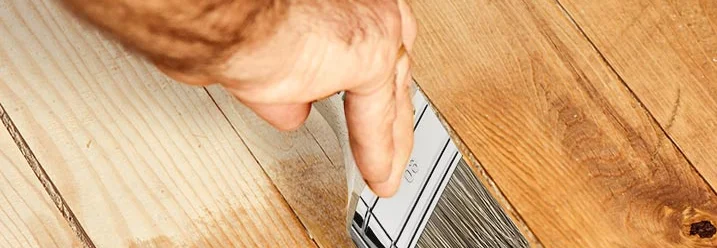 Person streicht Holzboden mit Pinsel