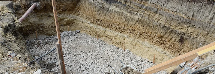 Ausgehobener Baugraben mit Kies und Schubkarre