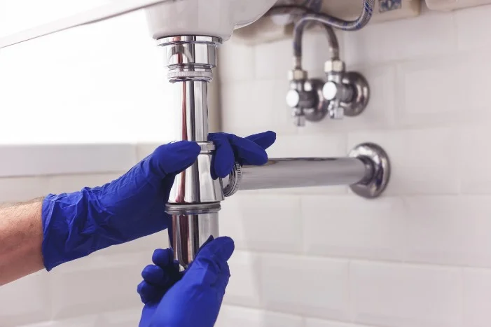 Hände mit blauen Handschuhen montieren einen Siphon