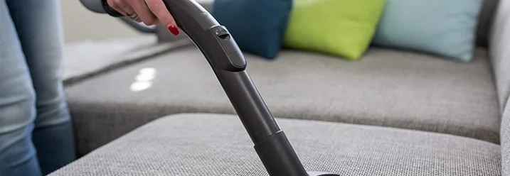 Person saugt Sofa mit Staubsauger