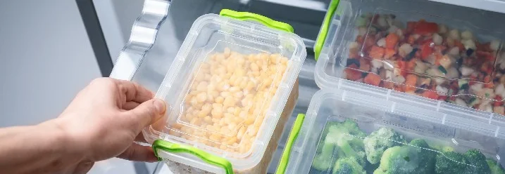 Hand nimmt Dose mit Mais aus Gefrierschrank