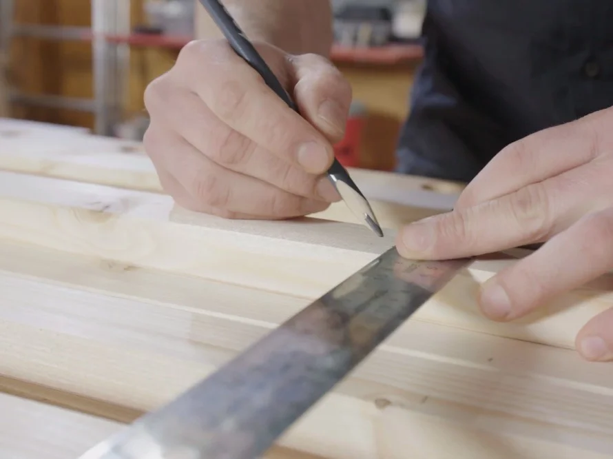 Person zeichnet Linie auf Holz mit Bleistift